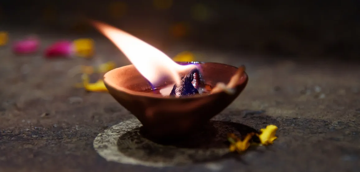 A small ceremonial flame in a clay bowl, surrounded by flower petals